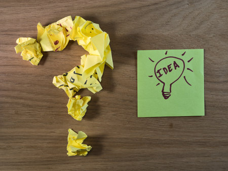 From Question to Bright Idea - A question mark made of crumpled yellow paper next to a green sticky note with a lightbulb drawing and "IDEA". Problem-solving concept.の写真素材