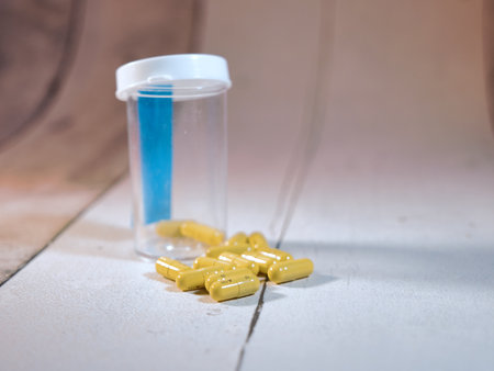 Spilled Yellow Capsules, Pill Bottle - Close-up of yellow capsule pills spilled from an empty prescription bottle on a textured white surface, symbolizing health, dosage, and medical care.の写真素材