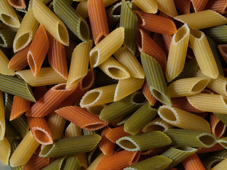 Tricolor Penne Pasta Macro Food Pattern - Close-up, full-frame background of raw, dry tricolor penne (macaroni) pasta in green, yellow, and red. Ideal for Italian food, cooking, and grain concepts.の写真素材