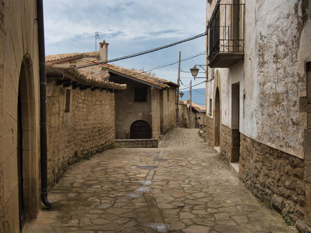 Ancient Stone Street in European Mountain Village - Historic cobblestone street lined with rustic stone houses and a balcony under a cloudy, atmospheric sky.の写真素材