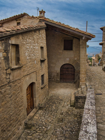 Ancient Stone Street in European Mountain Village - Historic cobblestone street lined with rustic stone houses under a cloudy, atmospheric sky.の写真素材