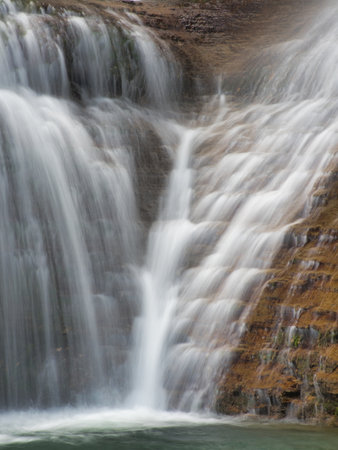 Close-up of Waterfall Cascading Down Rocks - Vertical shot using long exposure to create a silky, smooth effect of water rushing over textured, reddish-brown rock formations into a pool.の写真素材