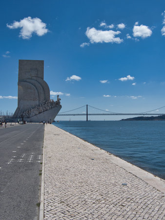 Discoveries Monument, Tagus River, Lisbon - The Padrão dos Descobrimentos monument on the Tagus riverfront, with the 25 de Abril Bridge and a clear blue sky in Lisbon, Portugal.の写真素材