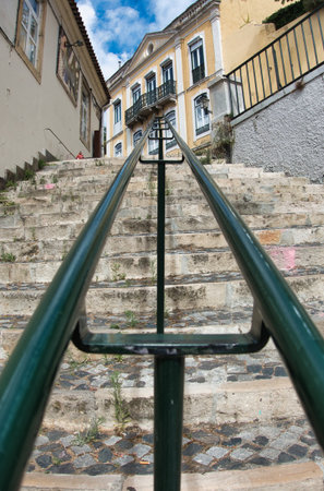 Historic Stone Stairs with Green Handrail - Low angle view of weathered stone stairs with a converging green metal railing leading up to a traditional European building facade in a historic city.の写真素材