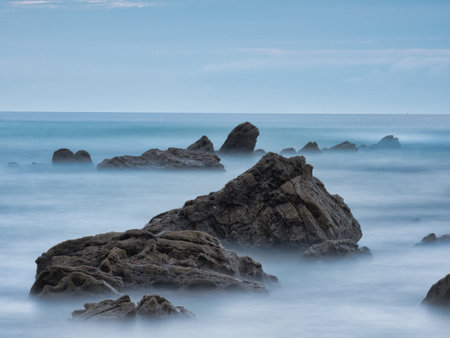 Striking Flysch Rock Leading Line Blue Hour Coast - Dramatic long exposure of a solitary flysch rock formation acting as a leading line towards the mountains under a cool blue hour sky.の写真素材