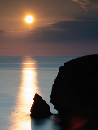 Vertical Sunrise Sunburst Over Coastal Cliff - Dramatic vertical long exposure capturing the sun and its intense reflection path on the ocean, silhouetting a large cliff and sea stack at sunrise.の写真素材
