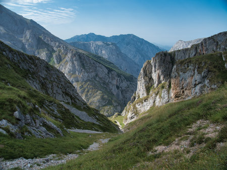 Deep Mountain Valley and Rugged Gorge Landscape View - Stunning vertical shot of a dramatic gorge and lush valley in the Picos de Europa, Spain, under a clear blue sky.の写真素材