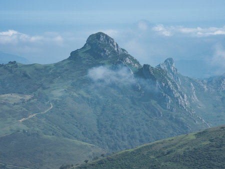 Misty Green Peak in Rolling Mountain Landscape - Serene view of a lush, verdant mountain and its rocky summit partially covered by low clouds or fog, promoting tranquility and nature.の写真素材