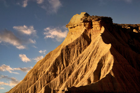 Abstract Desert Badlands Texture at Golden Hour - Striking close-up of eroded clay and sandstone peaks and ridges of badlands under harsh sidelight, creating strong diagonal shadows.の写真素材