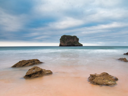 Coastal Sea Stack Monolith in Smooth Ocean - Long-exposure shot of a grass-topped sea stack monolith rising from the Atlantic Ocean, framed by smooth blurred water and rugged foreground rocks.の写真素材