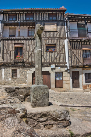 Traditional Half-Timbered Houses and Stone Cross - Historic Spanish village architecture featuring timber framing, white walls, and an ancient stone cross in the foreground.の写真素材