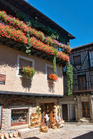 Traditional Village House with Flowered Balconies - Charming old stone house facade adorned with abundant red geranium flowers and rustic wooden balconies.の写真素材