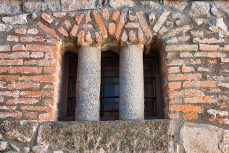 Ancient Window Detail with Twin Stone Columns - Close-up of a rustic brick and stone wall featuring a window separated by two small granite columns.の写真素材