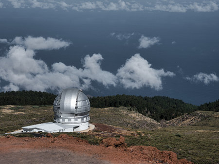 Silver Astronomical Observatory Dome on Mountain - High-altitude astronomical observatory with a silver dome on a mountain ridge, overlooking clouds and the ocean under a clear blue sky.の写真素材