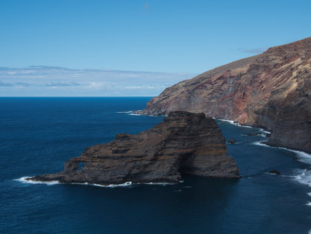Atlantic Coastal Cliffs with Rock Arch - Dramatic high-angle view of rugged volcanic cliffs meeting the deep blue Atlantic Ocean, featuring a prominent natural rock arch formation.の写真素材