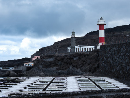 Lighthouse and Pink Salt Pans at Sunset - Striking coastal scene with the red and white lighthouse and old lighthouse overlooking salt evaporation ponds with pink water reflection on volcanic terrain.の写真素材