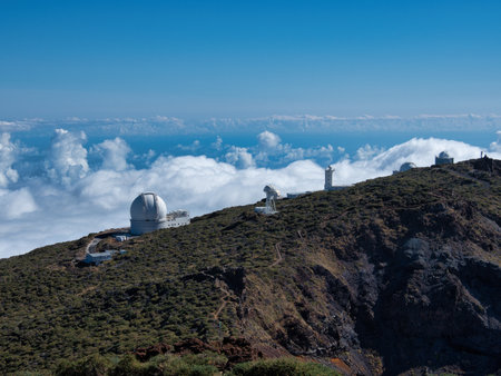Silver Astronomical Observatory Dome on Mountain - High-altitude astronomical observatory with a silver dome on a mountain ridge, overlooking clouds and the ocean under a clear blue sky.の写真素材