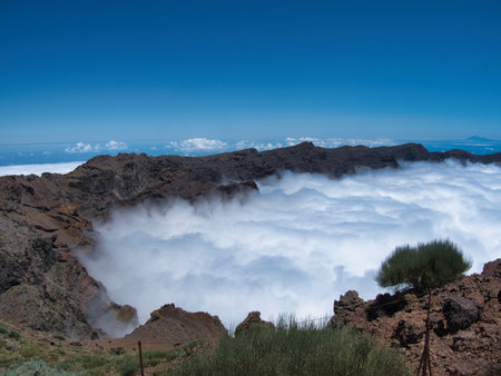 Volcanic Peak Overlooking White Cloud Sea - Expansive mountain landscape of red and gray volcanic rocks on a trail overlooking a vast, dense sea of white clouds under a deep blue sky.の写真素材