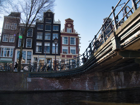 Dramatic Amsterdam Canal Perspective with Bridge - Low-angle shot of a metal canal bridge structure and traditional Dutch gable houses with parked bicycles under a blue sky.の写真素材