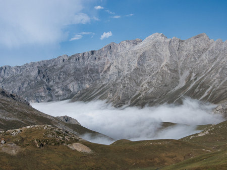 Dirt trail leading to majestic mountain view - Wide-angle shot of a rocky hiking trail leading to a high-altitude mountain panorama with mist and low clouds in the valley.の写真素材