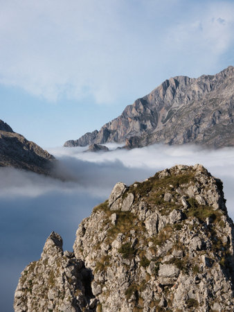 Misty valley and prominent mountain rock - Rugged mountain landscape with a cloud inversion filling the valley behind a large, textured rock formation in the foreground under a blue sky.の写真素材