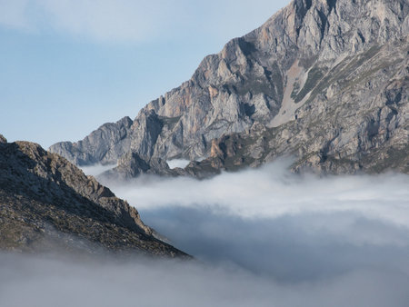 Dirt trail leading to majestic mountain view - Wide-angle shot of a rocky hiking trail leading to a high-altitude mountain panorama with mist and low clouds in the valley.の写真素材
