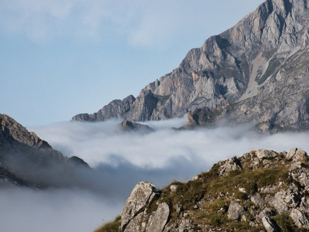 Misty valley and prominent mountain rock - Rugged mountain landscape with a cloud inversion filling the valley behind a large, textured rock formation in the foreground under a blue sky.の写真素材