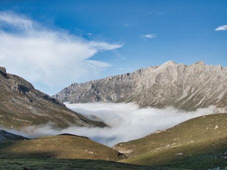 Dirt trail leading to majestic mountain view - Wide-angle shot of a rocky hiking trail leading to a high-altitude mountain panorama with mist and low clouds in the valley.の写真素材