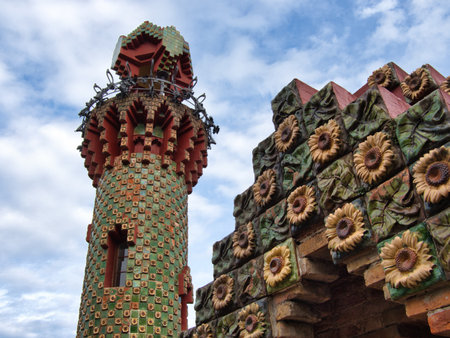 GaudÃ­-Style Modernist Tower and Sunflower Detail - Low-angle view of an elaborate ceramic-tiled tower and cornice featuring repeated sunflower reliefs and red brick.の写真素材