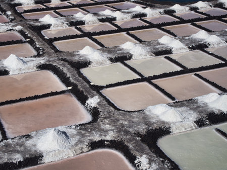 Abstract pattern of traditional salt evaporation ponds - High-angle, close-up view of geometric salt pans (salinas) with salt mounds and different colors of water and sediment under the sun.の写真素材