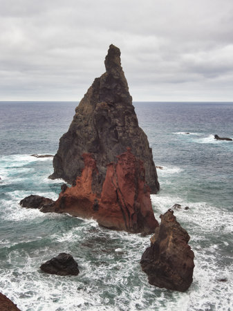 Majestic Sea Stacks of Madeira Coast - Dramatic view of volcanic sea stacks and red-hued cliffs at Ponta de SÃ£o LourenÃ§o, Madeira, with crashing waves under a cloudy sky.の写真素材