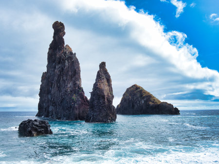 Powerful Volcanic Sea Stacks of Ribeira da Janela - Striking view of the IlhÃ©us da Ribeira da Janela volcanic sea stacks in Madeira, rising from the Atlantic Ocean under a bright blue sky with white clouds.の写真素材