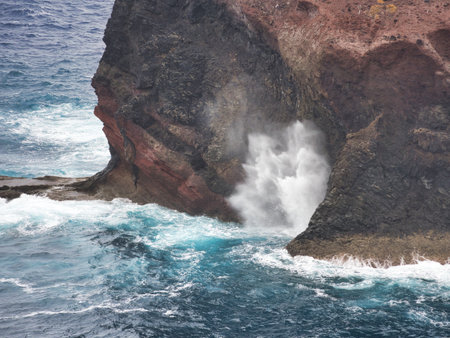 Dynamic close-up of a powerful ocean wave crashing into a volcanic sea cave or blowhole in Madeira, creating a dramatic spray of white water.の写真素材