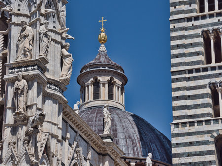 Siena Cathedral Dome, Campanile, and Facade Details - Close-up of the intricate architecture of Siena Duomo, showing the dome's lantern, striped bell tower, and ornate facade with statues against a clear blue sky.の写真素材