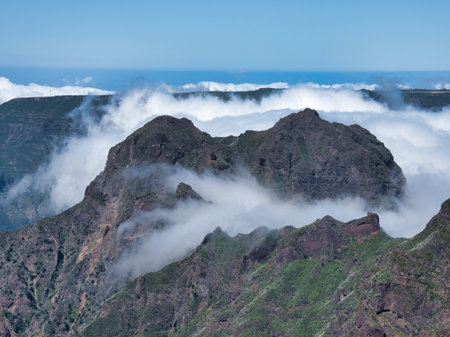 Madeira Volcano Peaks in Rolling Clouds - Dramatic wide shot of dark, rugged volcanic mountains partially submerged in a blanket of bright, low-rolling clouds.の写真素材