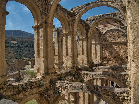 Arches of Medieval Monastery Ruins - Stone arches and columns of a derelict Gothic monastery against a blue sky, set in a mountainous Spanish landscape.の写真素材