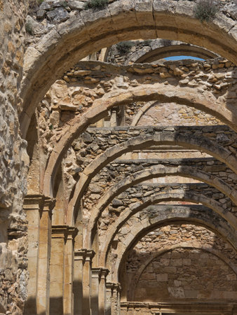 Arches of Medieval Monastery Ruins - Stone arches and columns of a derelict Gothic monastery against a blue sky, set in a mountainous Spanish landscape.の写真素材