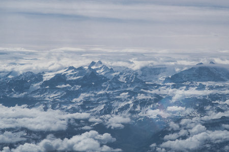Dramatic Snow-Covered Alps and Clouds - Stunning aerial view capturing the rugged, snow-covered mountain peaks of the Alps, emerging from a thick layer of swirling white clouds.の写真素材