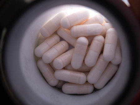 White Capsules in Medicine Bottle - Overhead view of numerous white pharmaceutical capsules inside a container, ideal for healthcare, medicine, supplements, and wellness themes.の写真素材