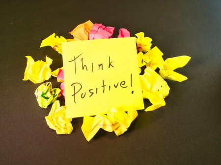 Think Positive! Motivation Note - Uplifting 'Think Positive!' message on a bright yellow note, contrasting with colorful crumpled paper on dark. Symbolizes optimism and resilience.の写真素材