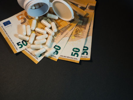Healthcare Costs: Euro Banknotes & Pills - White capsules spill from an open bottle onto fanned 50 Euro banknotes, illustrating the escalating costs of medication and healthcare expenses.の写真素材