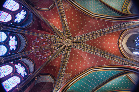 Gothic Vaults and Murals of Sainte-Chapelle - Low-angle view of richly painted Gothic rib vaulting in red, gold, and teal, alongside a large crucifixion mural and stained glass windows.の写真素材