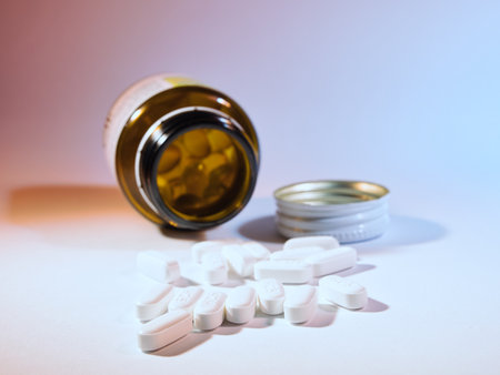 Pills and Medicine Bottle Spilled - White oval pills spilled from an amber medicine bottle with a cap on a soft gradient background. Concepts of health, pharmacy, and medication.の写真素材