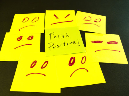Think Positive Among Negativity - A motivational message to "Think Positive!" stands out amidst a collection of yellow sticky notes depicting various negative emotions and frowns.の写真素材