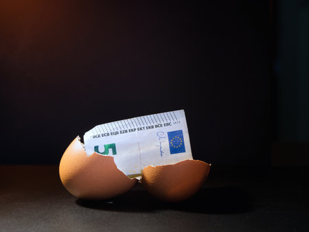 Euro Banknote in Cracked Eggshell - A five Euro banknote emerging from a cracked eggshell on a dark background, symbolizing financial growth, savings, and new beginnings.の写真素材