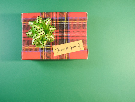 Plaid Gift with Thank You Note - Overhead view of a plaid gift box tied with a green polka dot bow and a 'Thank you' note on a vibrant green background, perfect for gratitude.の写真素材