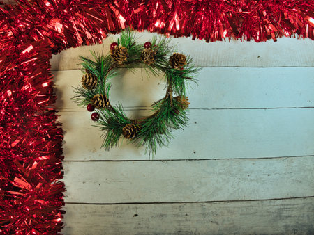 Rustic Christmas Wreath & Red Tinsel - Festive Christmas wreath with pinecones and red berries framed by red tinsel on rustic white wooden background, perfect for holiday greetings or promotions.の写真素材