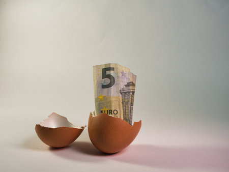 Five Euro banknote rising from a broken chicken eggshell on a plain background, symbolizing...