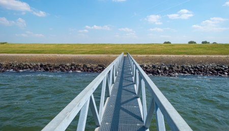 Sunlit footbridge over a lake to a damの写真素材