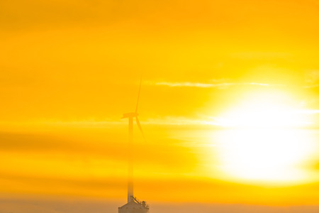 Wind turbine in a foggy field at sunrise